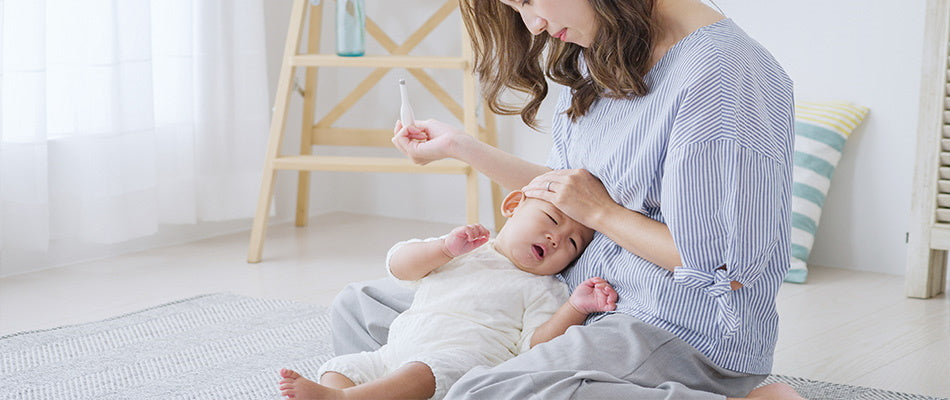 Eine Mutter misst Fieber bei ihrem schlafenden Baby, während sie ihm sorgenvoll die Stirn fühlt.