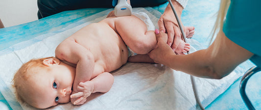 Ein Baby liegt auf einer Untersuchungsliege, während ein Arzt eine Ultraschalluntersuchung durchführt.