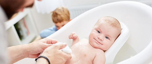 Ein Baby wird in einer Babybadewanne gebadet. Es lächelt und sieht zufrieden aus.