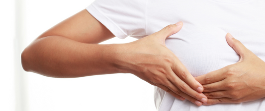 Eine Frau hält ihre Brust mit beiden Händen und trägt ein weißes T-Shirt. Sie drückt vorsichtig ihre Brust.