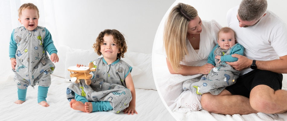 Links stehen und sitzen zwei Kinder in grauen Schlafsäcken mit blauen Ärmeln und Beinen auf einem weißen Bett. Eines der Kinder hält ein Spielzeugflugzeug.