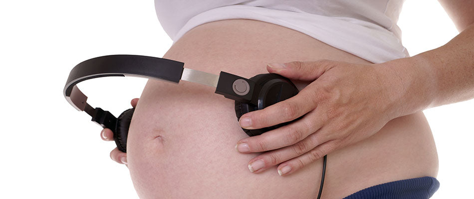 Schwangere Frau hält Kopfhörer an ihren Bauch, um dem Baby Musik vorzuspielen.