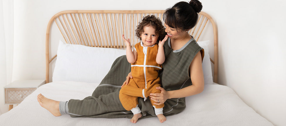 Eine Mutter und ihr Kind sitzen auf einem Bett und tragen Schlafsäcke mit Beinen.