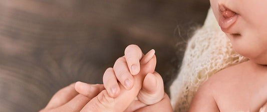 Neugeborenes zeigt Greifreflex, indem es den Finger eines Erwachsenen festhält.