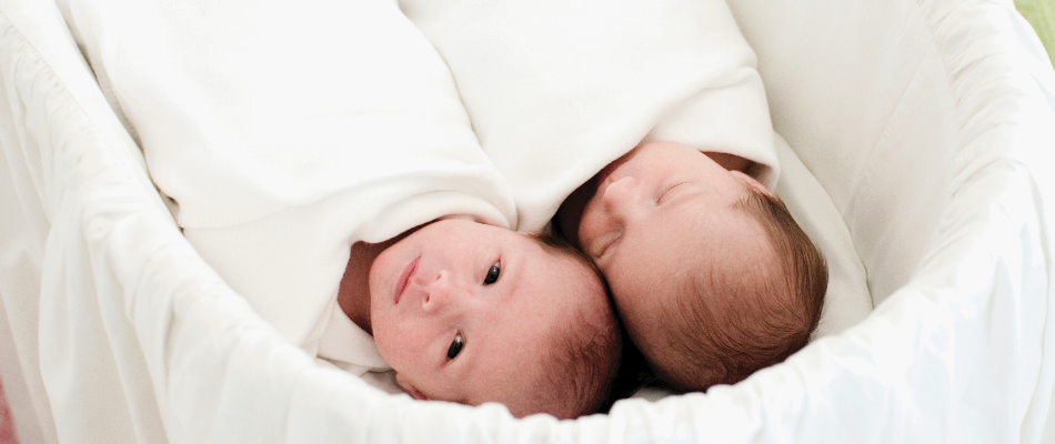 Zwei Neugeborene liegen nebeneinander in einem weißen Babybett, eingewickelt in weiße Decke - Schlaf von Zwillingenn