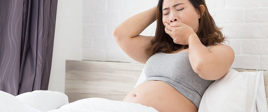 Eine schwangere Frau sitzt im Bett und gähnt, offenbar müde und schlaflos.