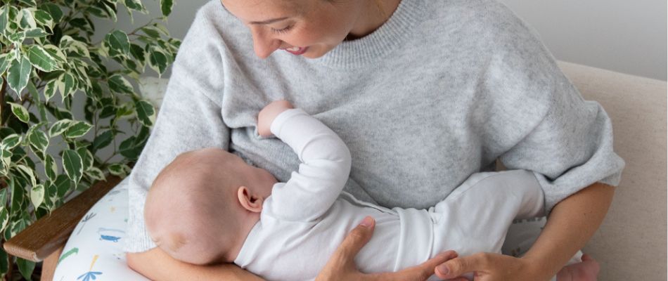 Eine Mutter stillt ihr Baby, das auf einem Stillkissen liegt. Sie lächelt liebevoll und hält das Baby sanft im Arm.