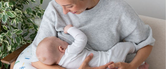 Eine Mutter stillt ihr Baby, das auf einem Stillkissen liegt. Sie lächelt liebevoll und hält das Baby sanft im Arm.