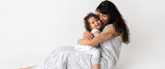 Eine Mutter sitzt auf dem Boden und umarmt ihr lachendes Kind, beide tragen passende Kleidung.