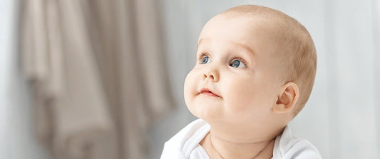 Ein Baby mit großen, blauen Augen schaut aufmerksam nach oben.