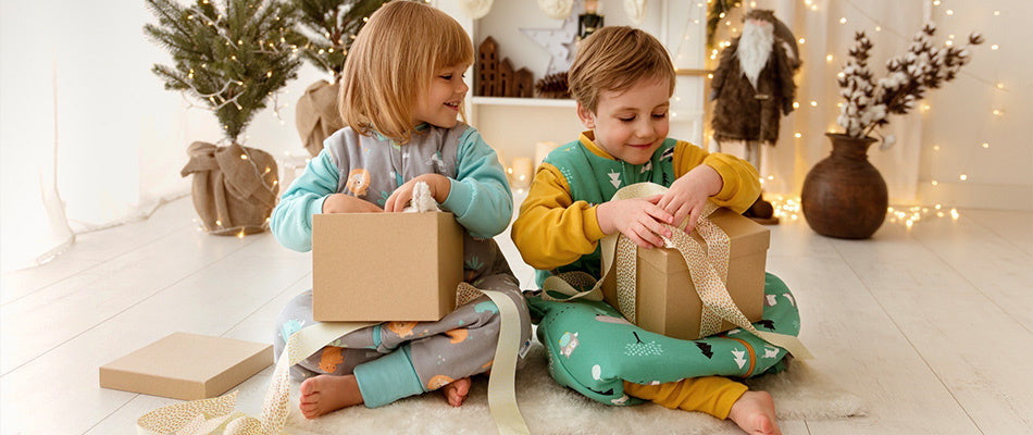 Zwei Kinder öffnen Weihnachtsgeschenke vor einem geschmückten Baum in festlicher Umgebung.