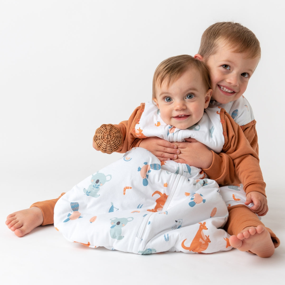 Zwei Kinder sitzen fröhlich auf dem Boden in Schlafsäcken mit Füßen. Sie lachen und spielen miteinander.